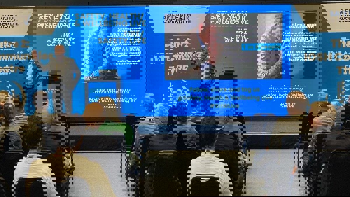 A speaker addresses the audience while a slide displays a statistic about global mental health conditions with an image of a distressed person.