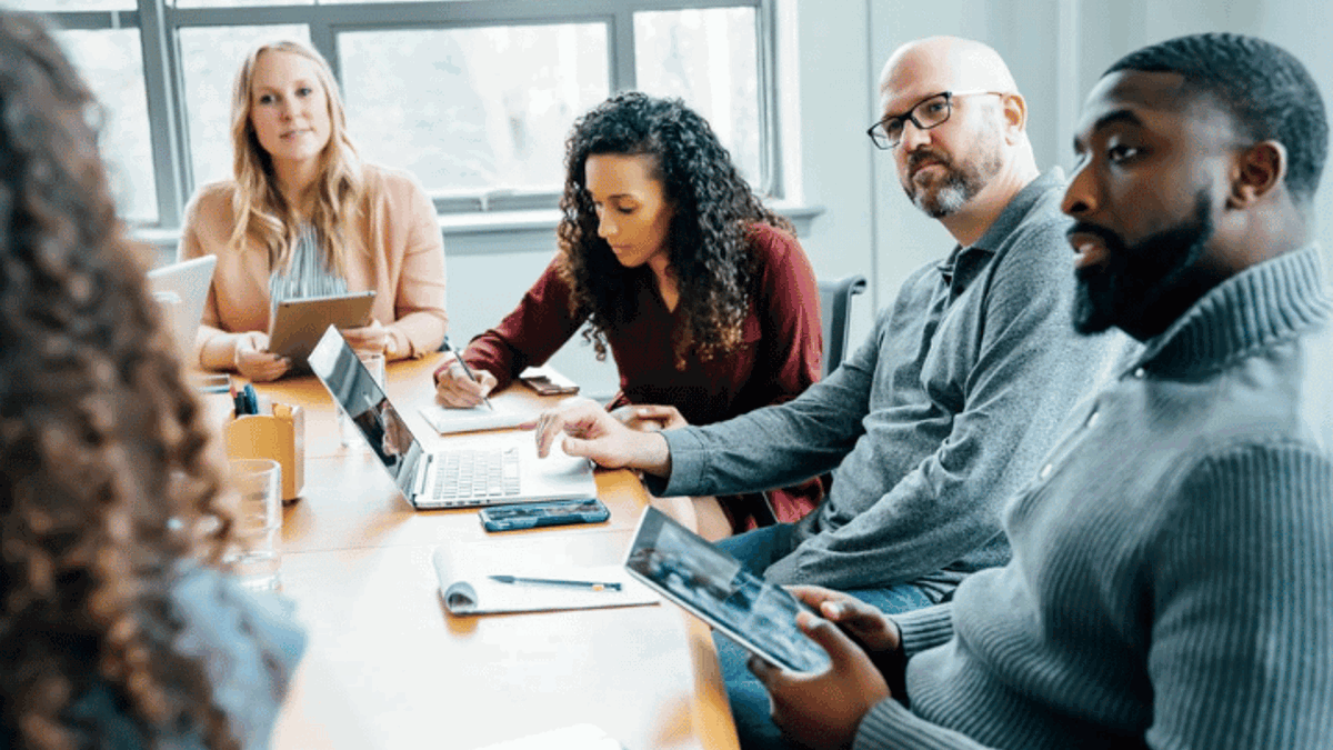 Diverse group of people sitting round a desk in discussion
