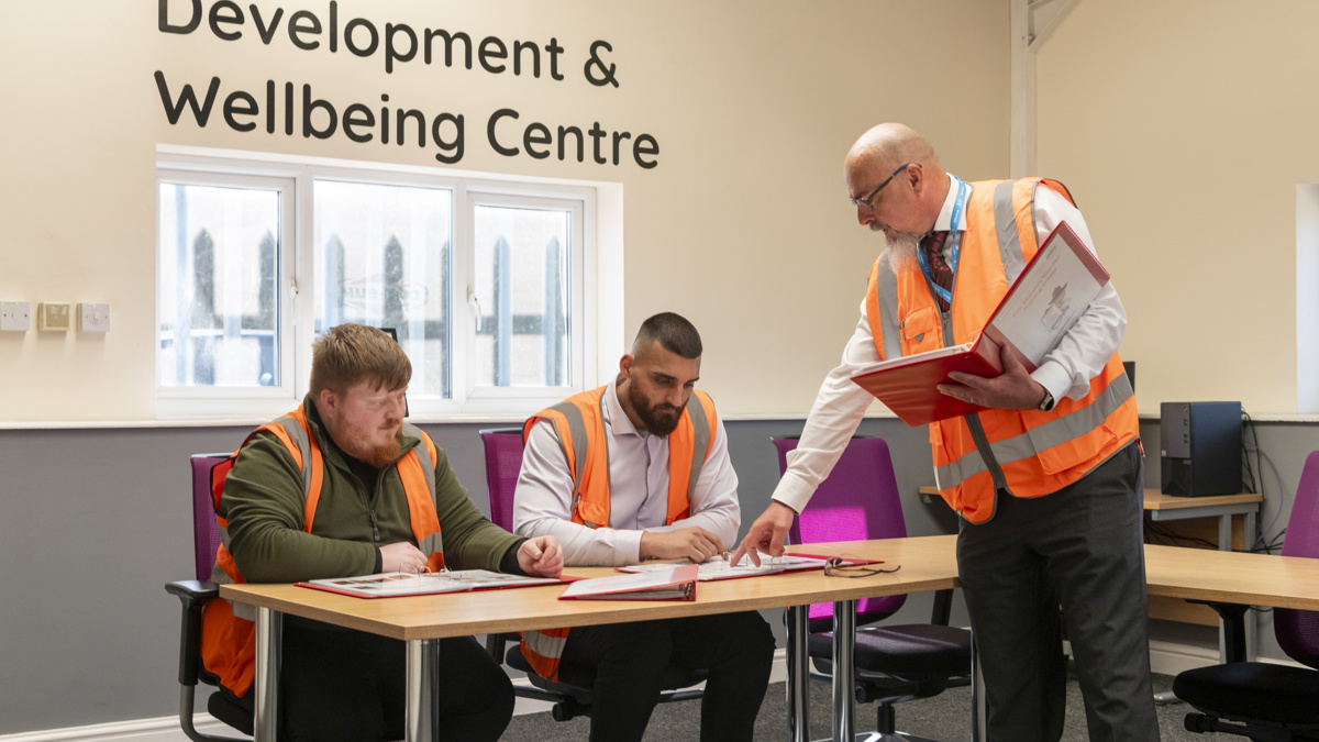Person in a high-visibility vest reviewing documents with two colleagues during a training session in the Don-Bur Development and Wellbeing Centre.