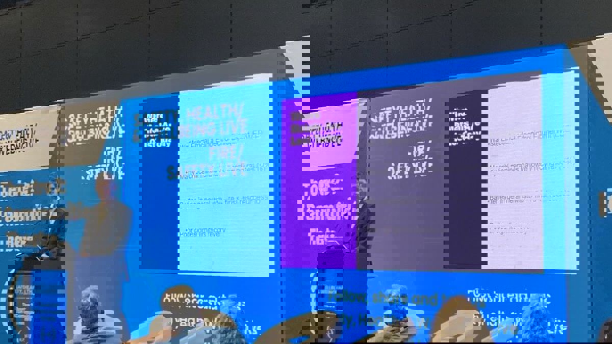A presenter stands beside a slide listing ways metals are lost in waste streams, including battery disposal.
