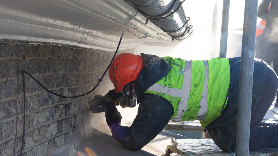 Workman using grinder with hard hat and respirator