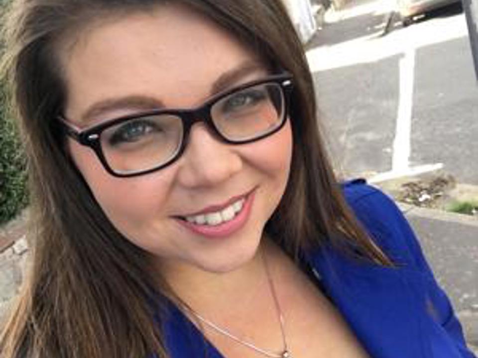 Kate Wilkinson wearing a blue smart blazer, smiling at the camera taking a selfie photo
