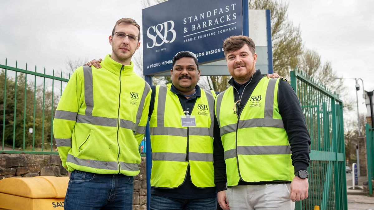 Chandrasekhar Shajahan and two colleagues in front of Standfast and Barracks sign