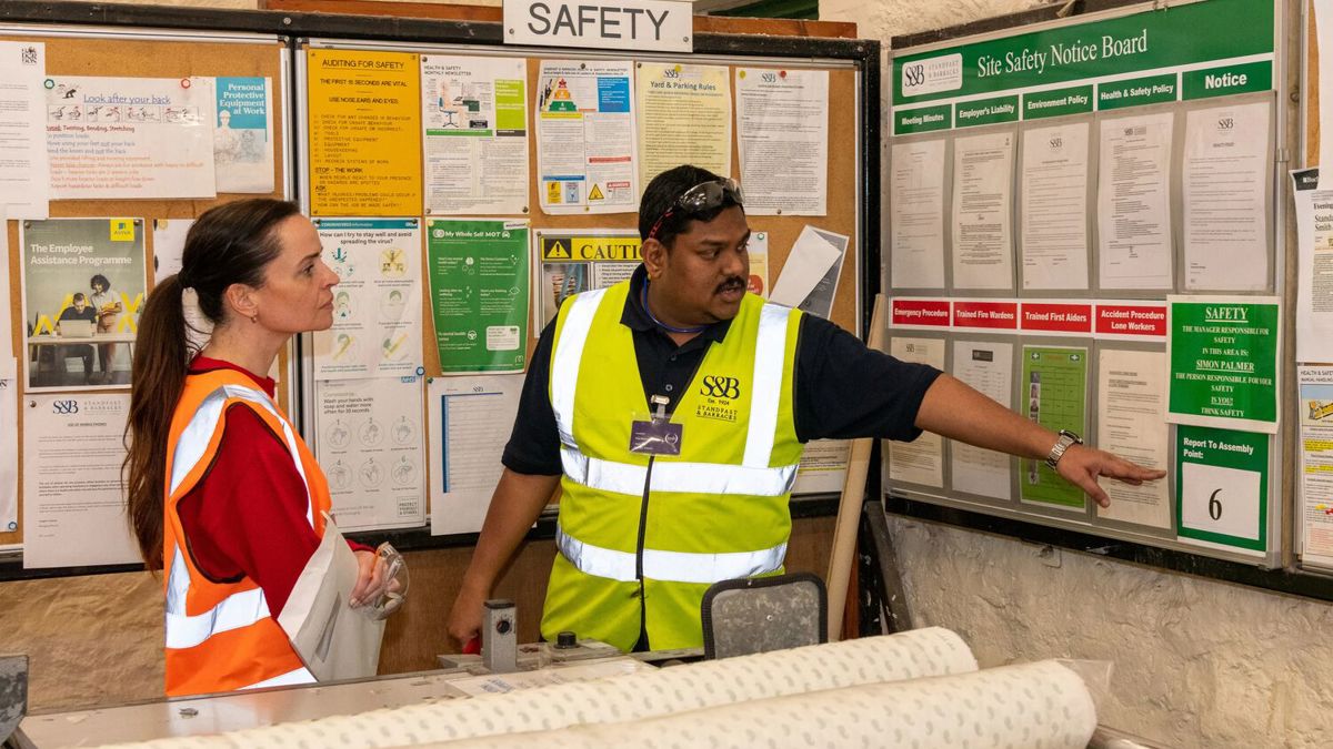 Chandrasekhar Shajahan pointing at factory message board and talking to a visitor