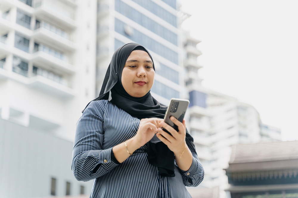 Woman in headscarf using tablet computer outside tall white building