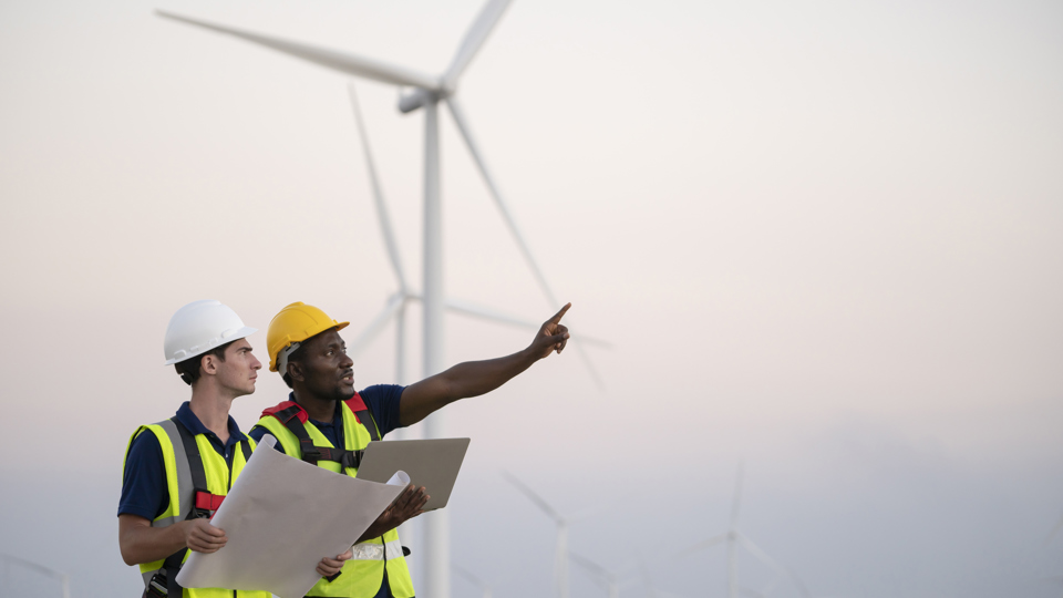 Two windfarm workers in discussion with turbines in the background
