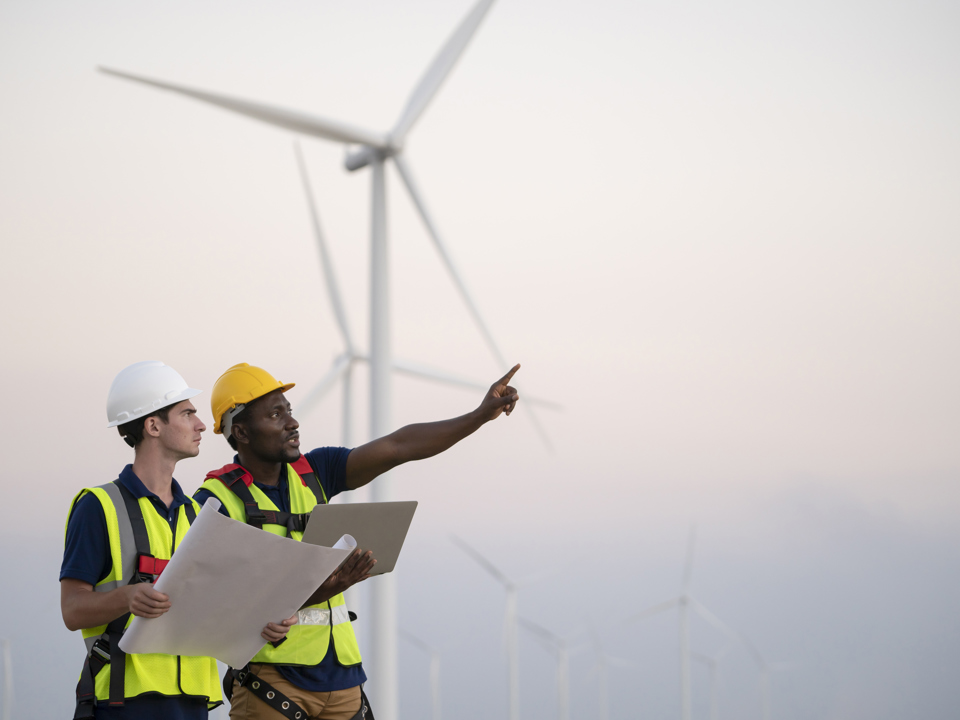 Two windfarm workers in discussion with turbines in the background