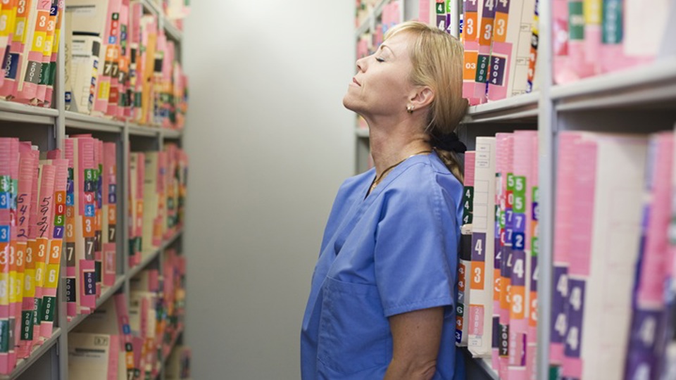 Healthcare worker standing between two bookcases of records looking stressed