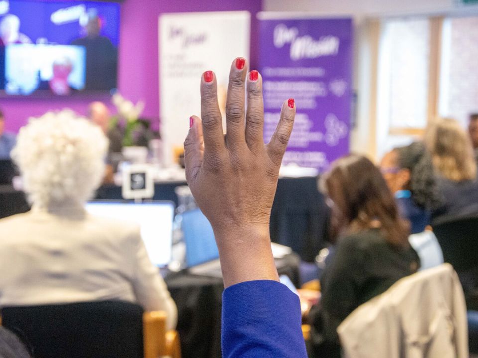 Person with red fingernails raising hand during meeting