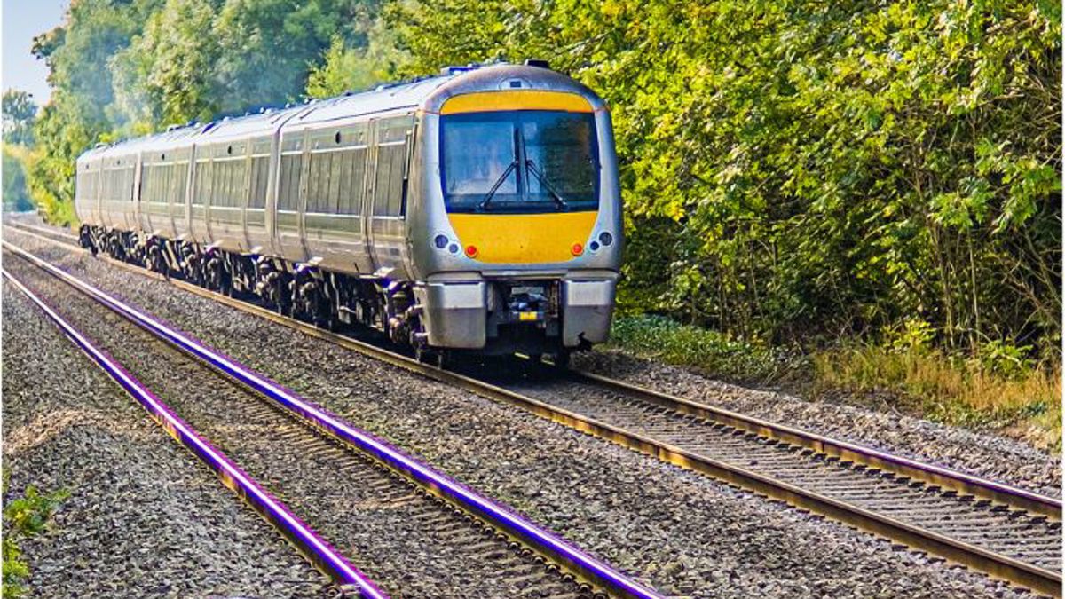 A passenger train travelling along a double‑track railway line surrounded by trees and greenery.