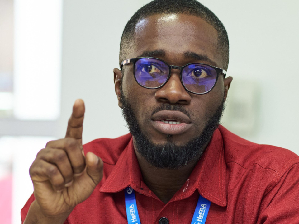 A person in a red shirt leans over a laptop during a session, with others seated at a table in a conference-style room and HeFRA branding visible in the background.