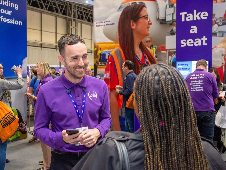 A man in an IOSH shirt talking to a woman with braided hair at a conference
