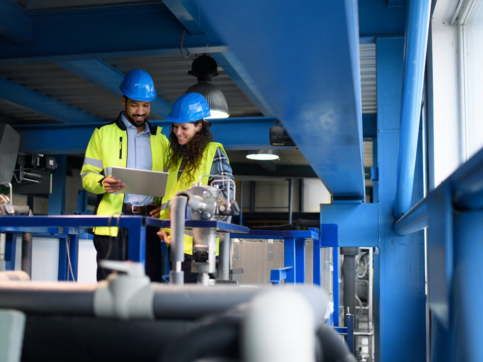 Two factory workers in high-vis jackets and hard hats