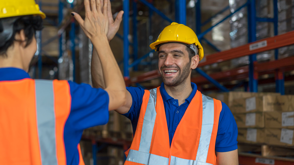 Male worker in hi-vis vest and hard hat high-fiving a colleague