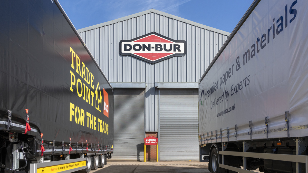 Two Don-Bur trailers parked outside an industrial building with the Don-Bur logo above a loading bay entrance.