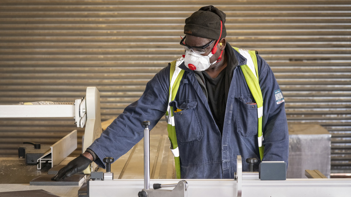 Employee wearing protective equipment, including a high-visibility vest, safety glasses and respiratory mask, operating machinery on the Don-Bur shop floor.