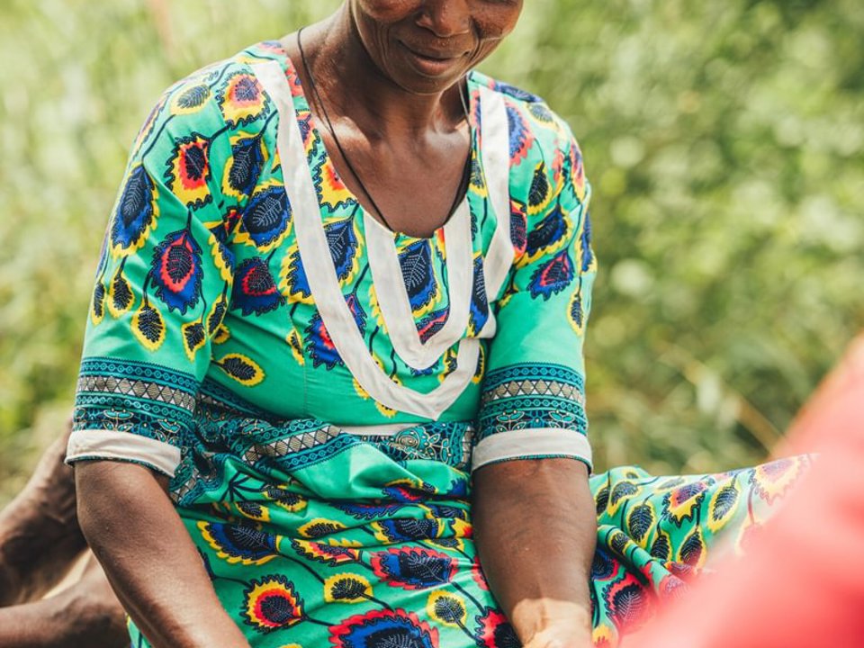 A female worker using a large stone to grind shea butter nuts