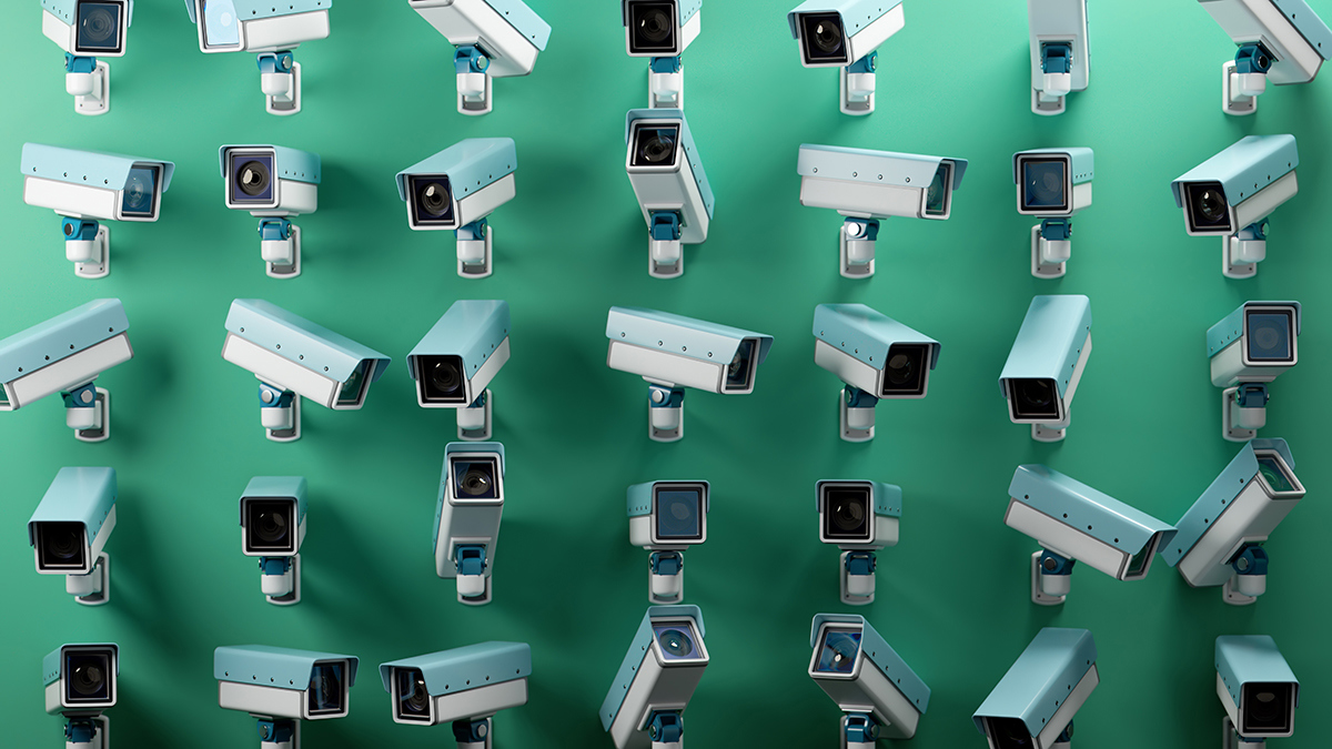 Multiple CCTV and surveillance cameras mounted against a green background, positioned at different angles to create a pattern representing monitoring, security and workplace technology.