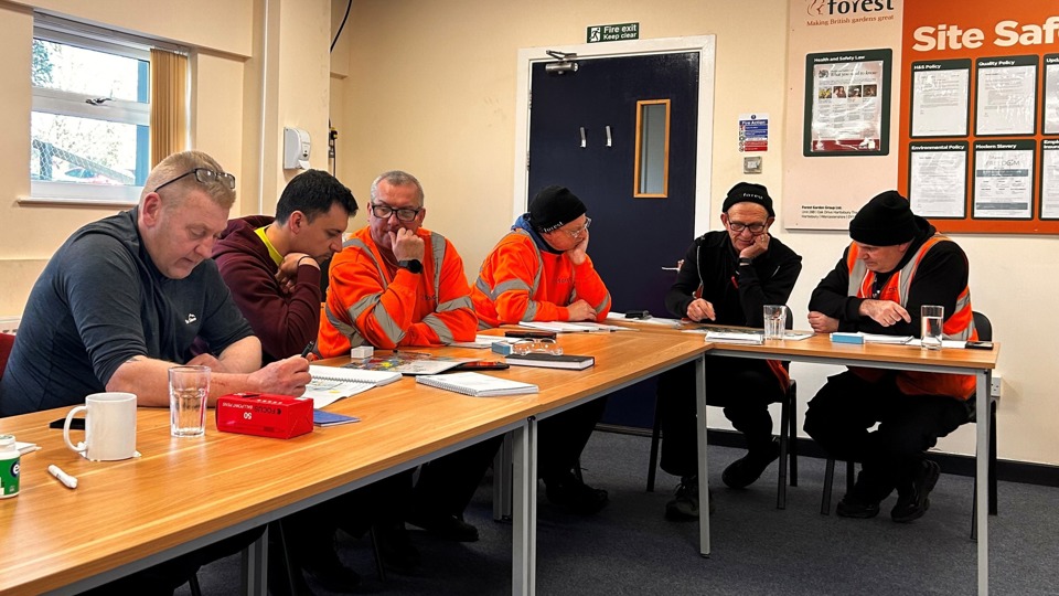 A group of six men sitting at desks and concentrating on a written exercise